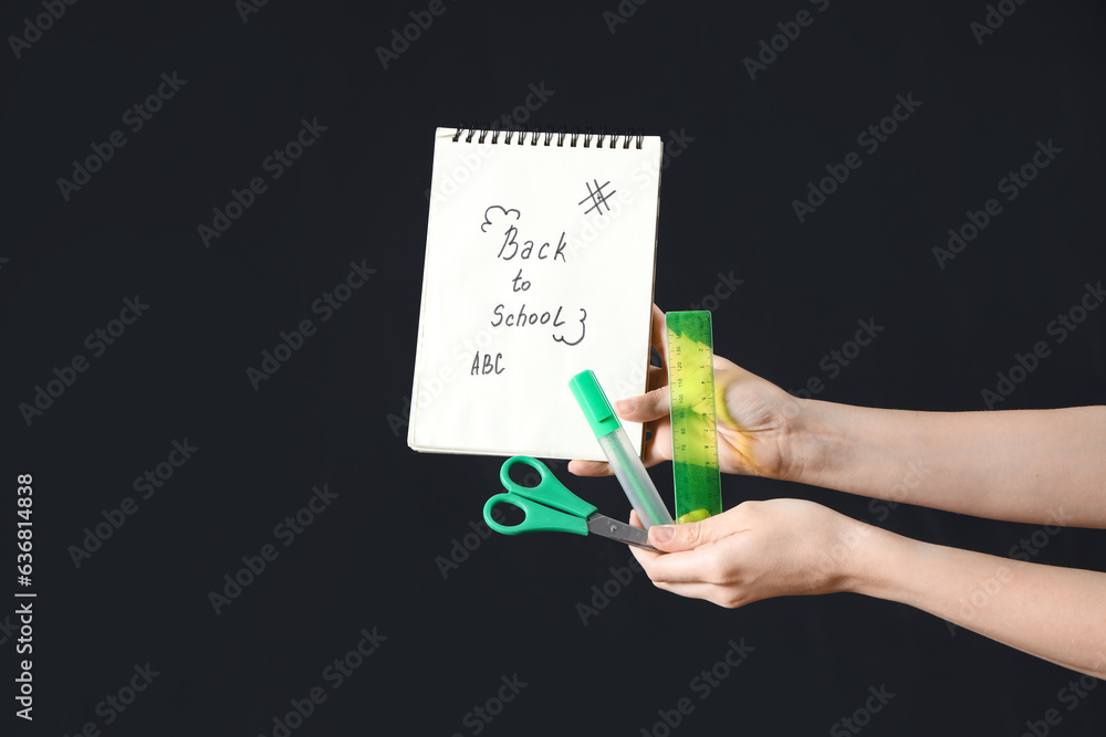 Female hands holding different stationery and notebook with text BACK TO SCHOOL on black background