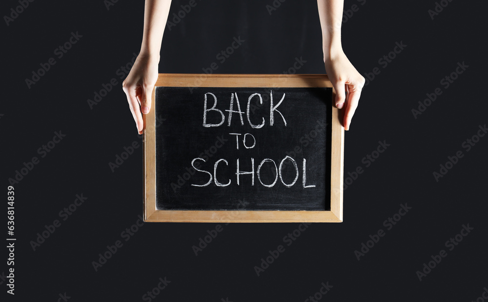 Female hands holding blackboard with text BACK TO SCHOOL on black background