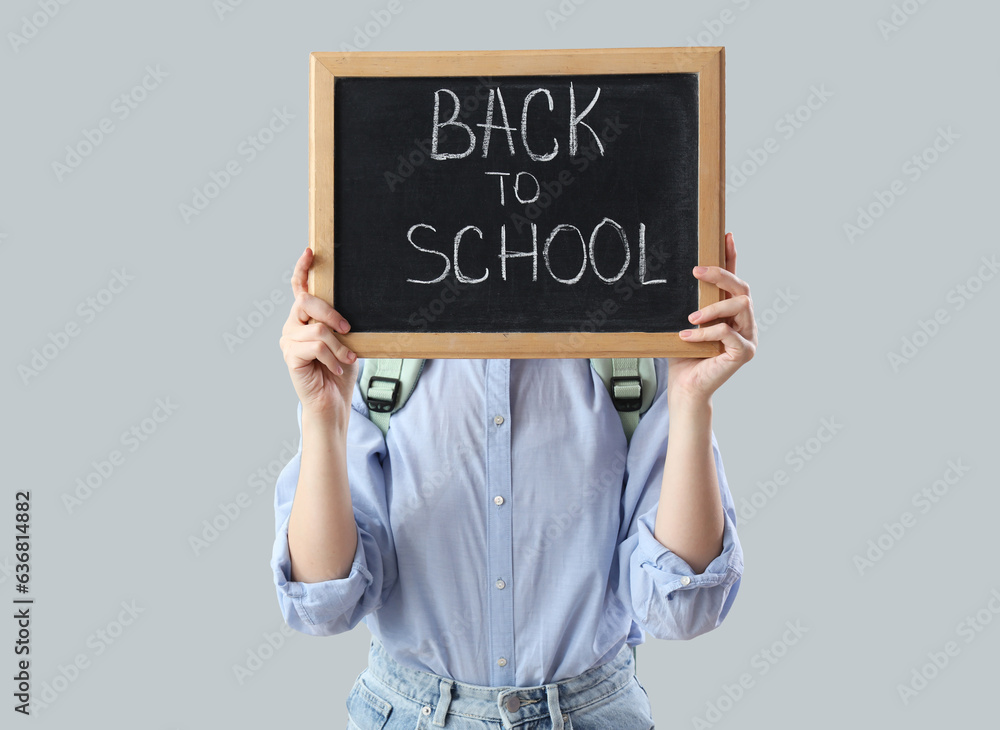 Schoolgirl in backpack holding blackboard with text BACK TO SCHOOL on grey background