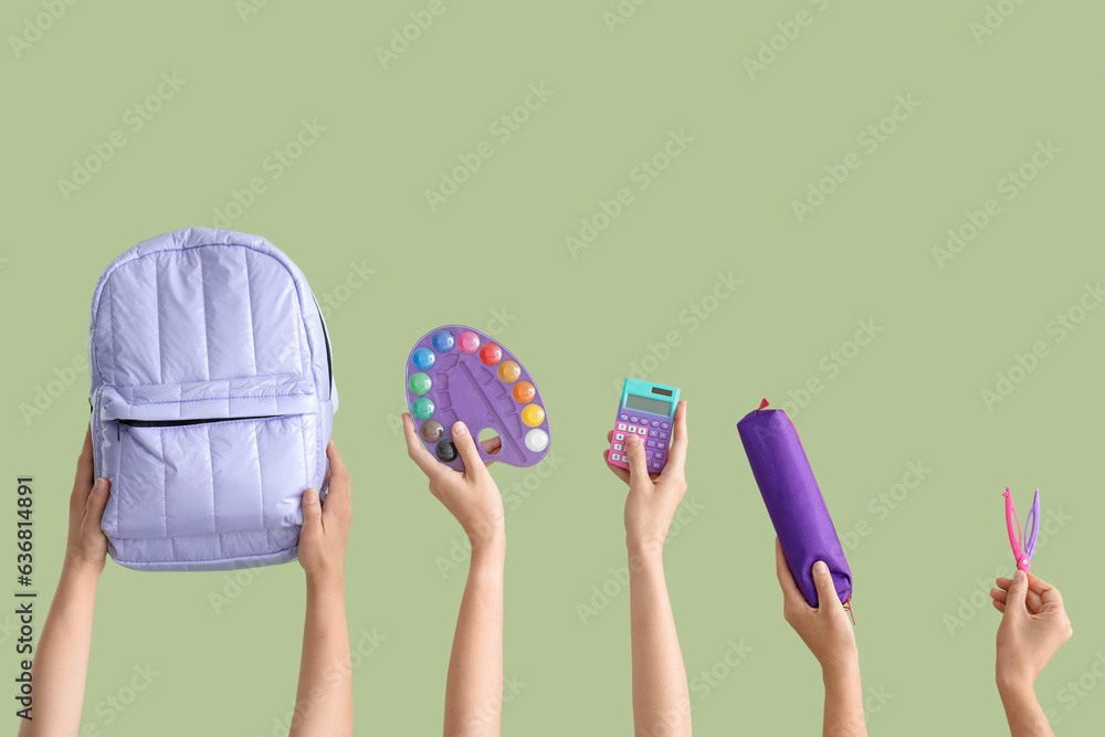 Female hands with backpack and different stationery on green background