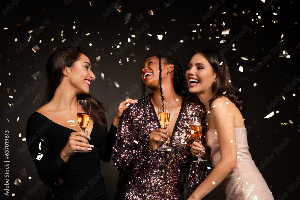 Three beautiful young ladies in nice dresses drinking champagne, laughing