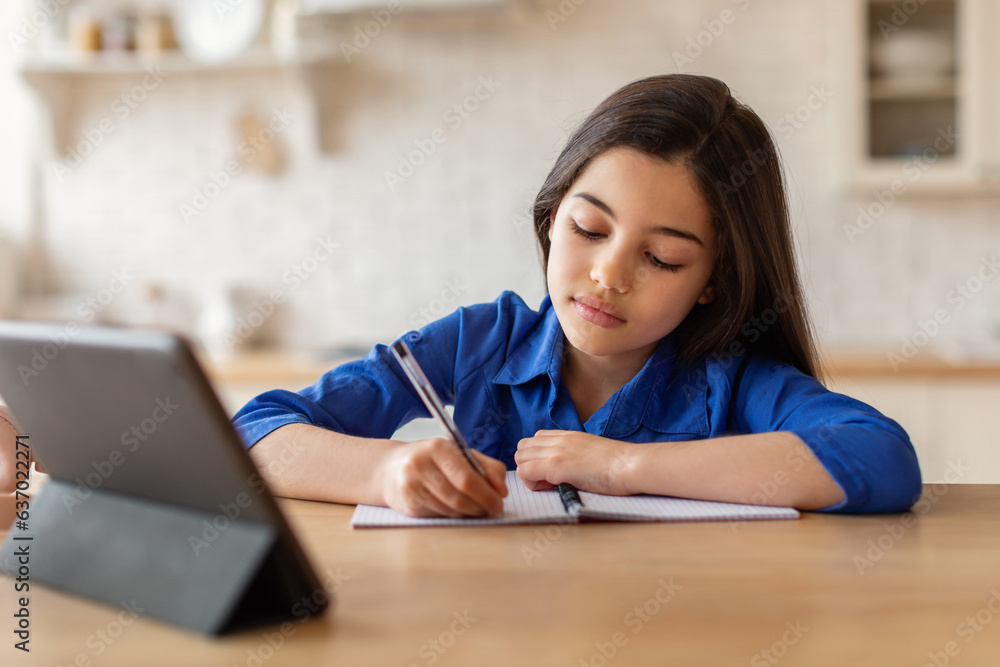 Girl studying at digital tablet writing in notebook at home