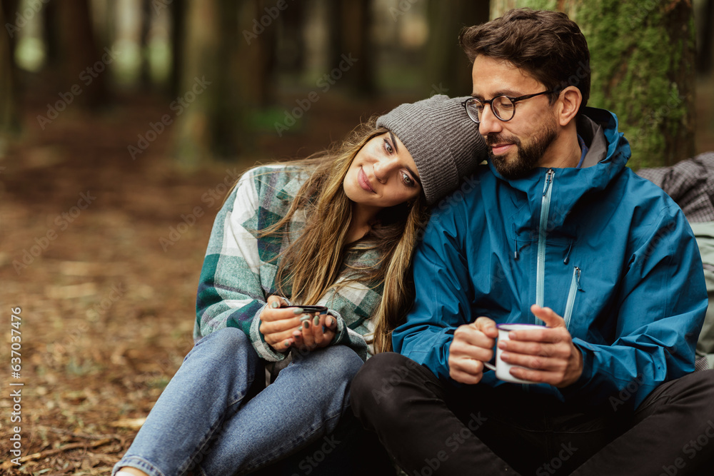 Relaxed happy young caucasian couple in jackets with cups of tea from thermos, enjoy travel, vacatio