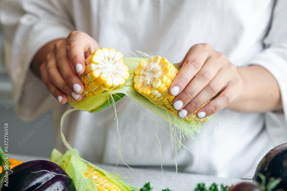 Close-up, raw corn in female hands in the kitchen.