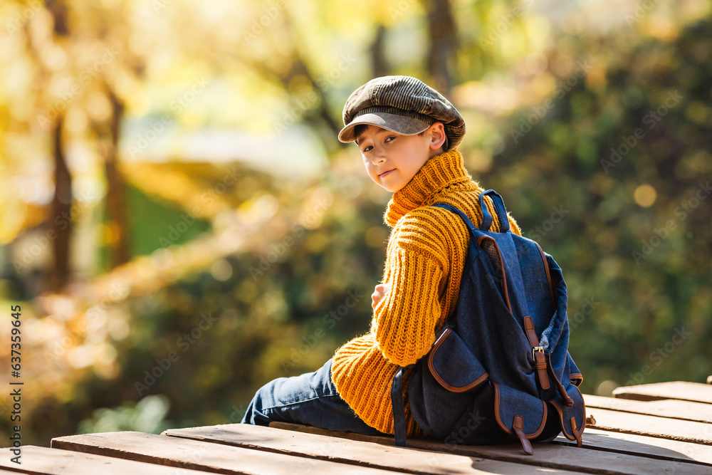 Portrait of a little boy in retro clothes with a backpack in autumn.