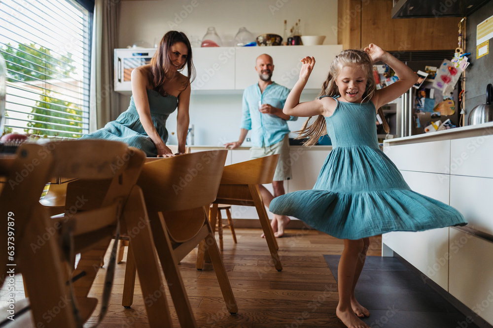 Little girl dancing in the kitchen, while parents watching her.