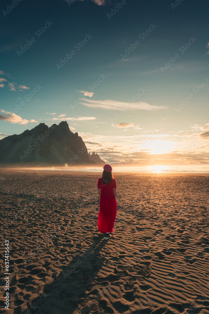 A woman standing with sunlight glowing in Vestrahorn mountain on black sand beach in Stokksnes penin