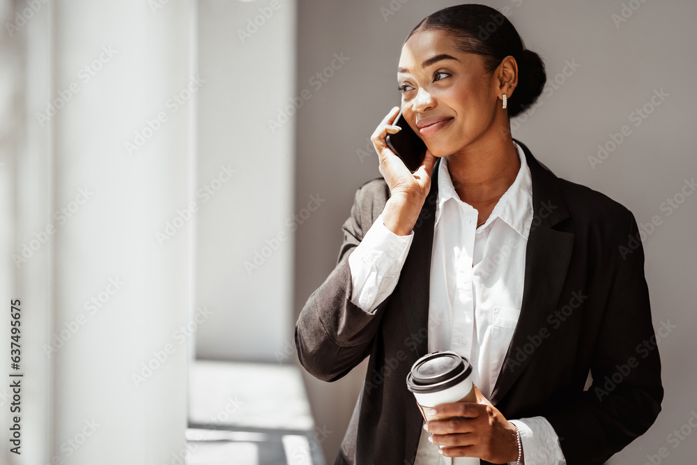 Happy attractive black lady entrepreneur drinking takeaway coffee and talking on phone in office, co