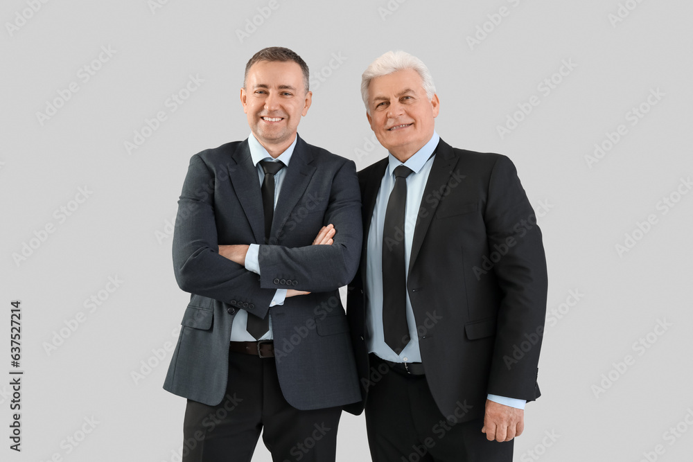 Mature brothers in suits on grey background