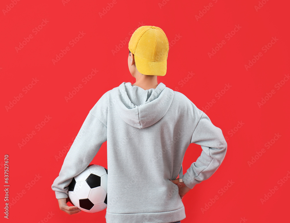 Little boy with soccer ball on red background, back view