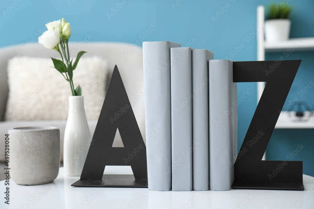 Stylish holder for books with vase of roses on table in room