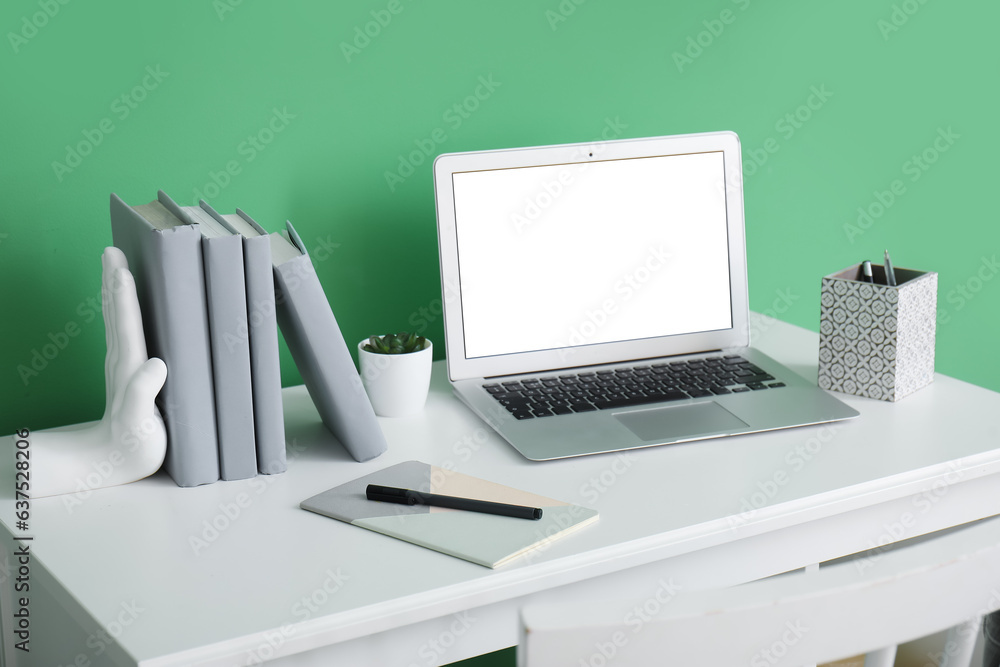 Stylish holder for books with computer on table near green wall