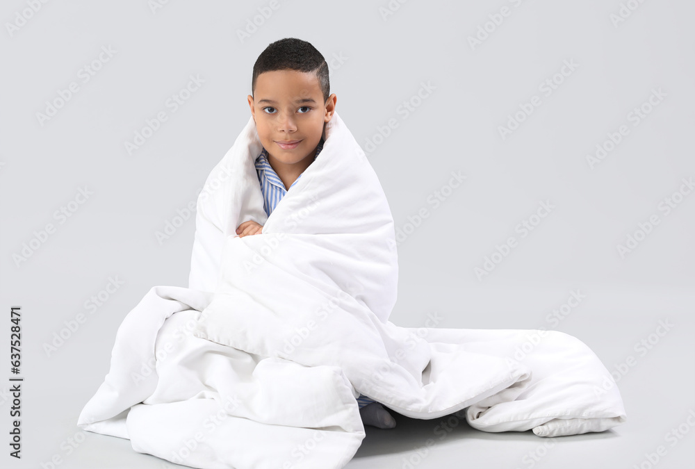 Little African-American boy with soft blanket sitting on light background