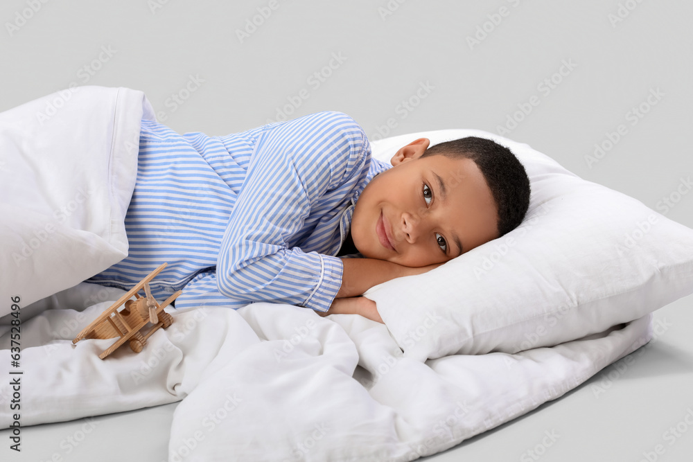 Little African-American boy with soft blanket lying on light background