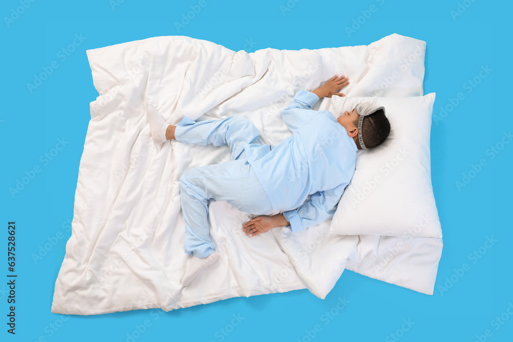 Little African-American boy with soft blanket sleeping on blue background, top view