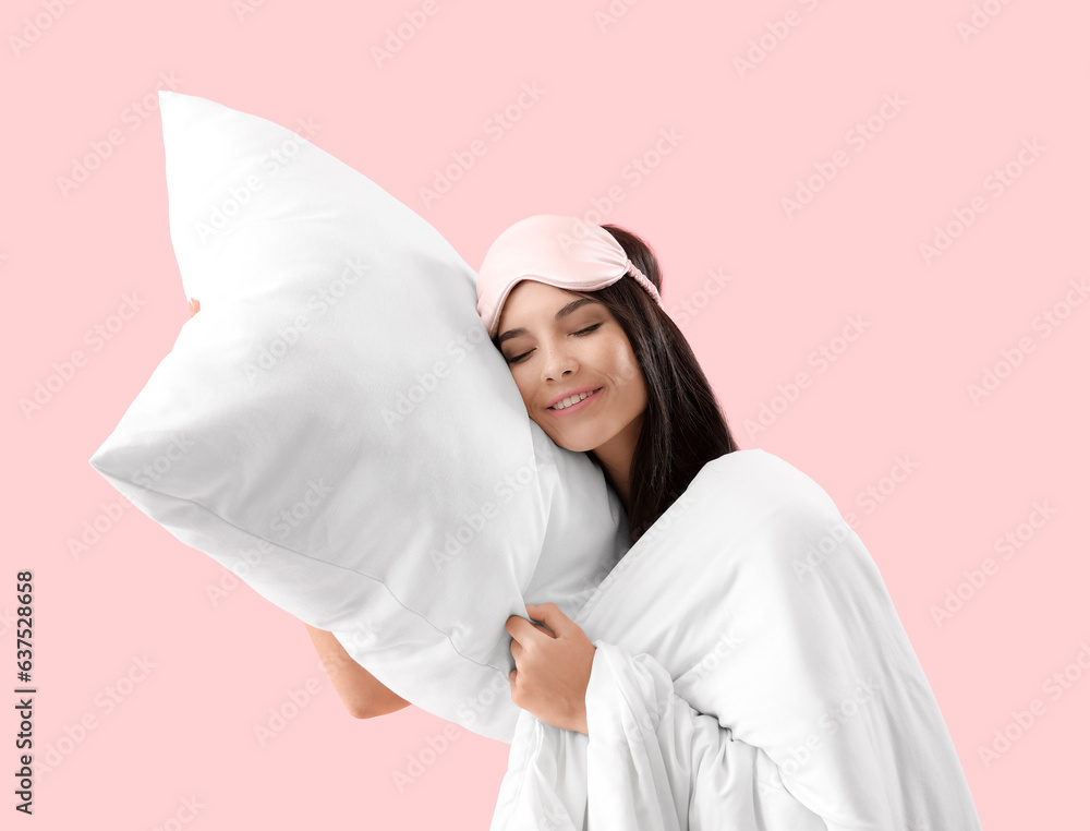 Beautiful young woman with soft pillow and blanket sleeping on pink background