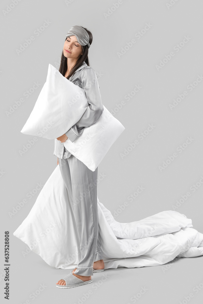 Beautiful sleepy young woman with soft blanket and pillow on grey background