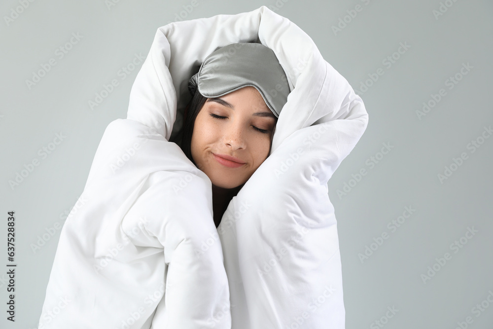 Beautiful young woman wrapped in soft blanket sleeping on grey background