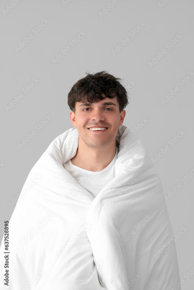 Handsome happy man wrapped in soft blanket on grey background