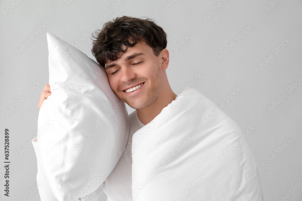 Handsome happy man with soft blanket and pillow sleeping on grey background