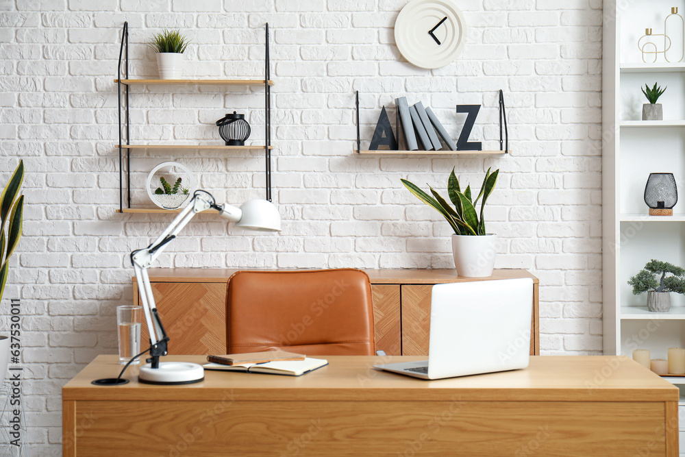 Workplace with laptop, stylish holder for books and lamp in room