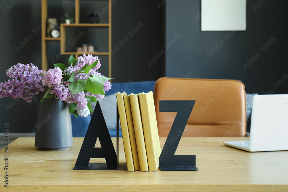 Stylish holder for books and vase of lilac flowers on table in room