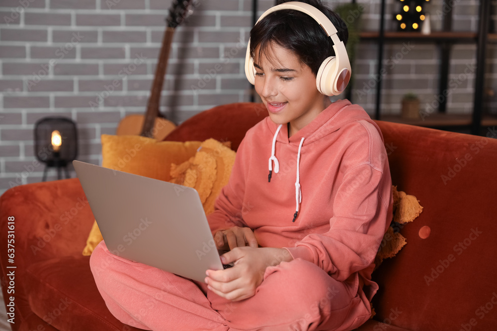 Little boy with headphones using laptop at home late in evening