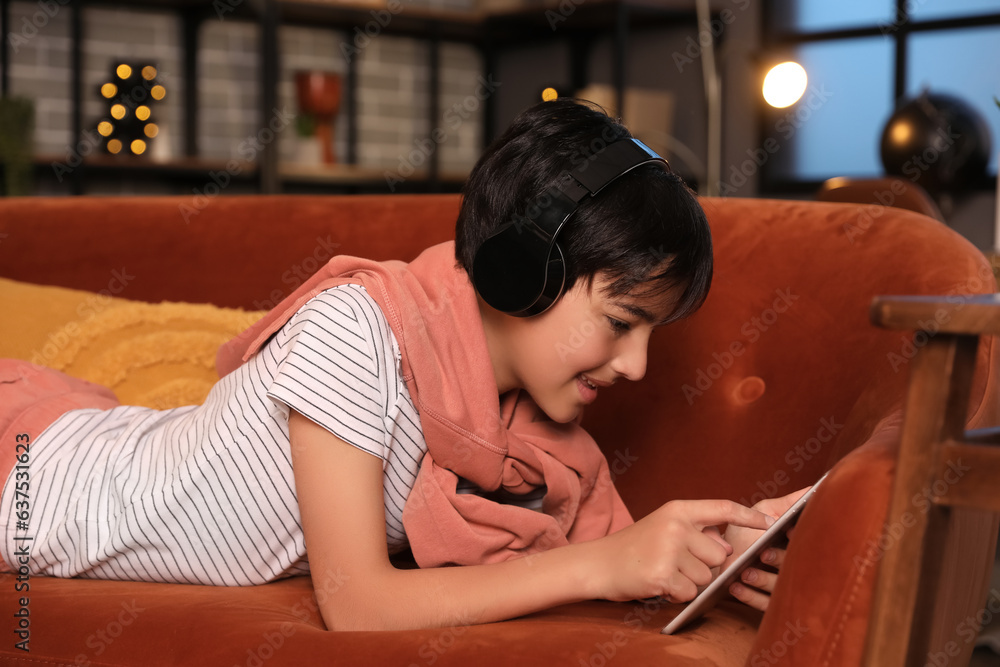 Little boy with headphones using tablet computer at home late in evening