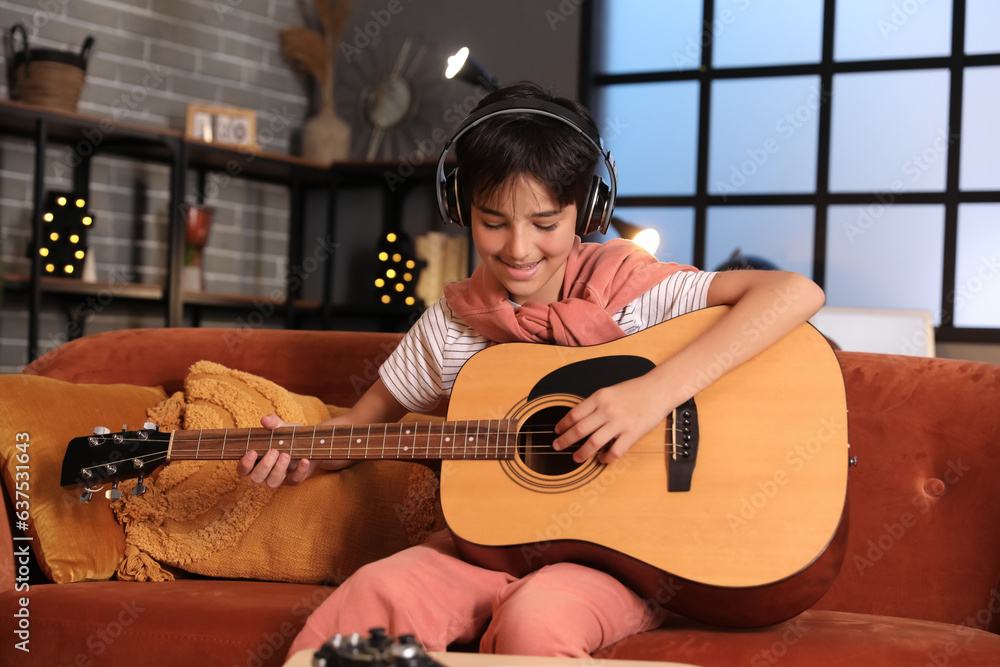 Little boy with headphones playing guitar at home late in evening