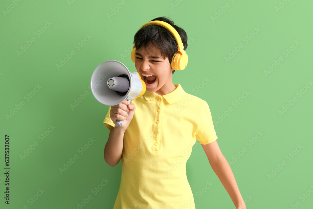 Little boy with headphones shouting into megaphone on green background