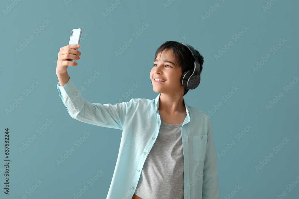 Little boy in headphones with mobile phone taking selfie on blue background