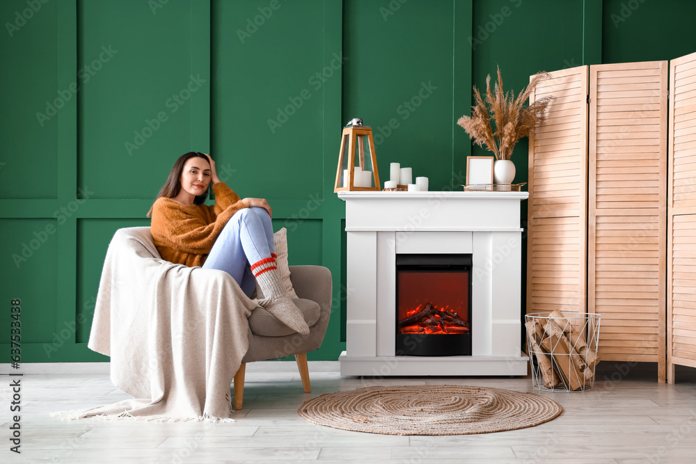 Young woman sitting in armchair near fireplace at home