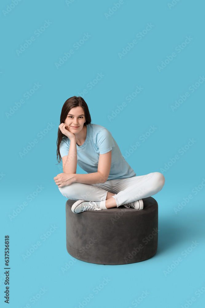 Young woman sitting on pouf against blue background