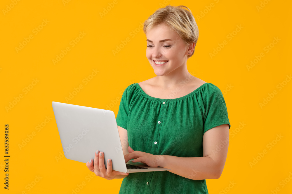 Happy young female programmer with laptop on yellow background