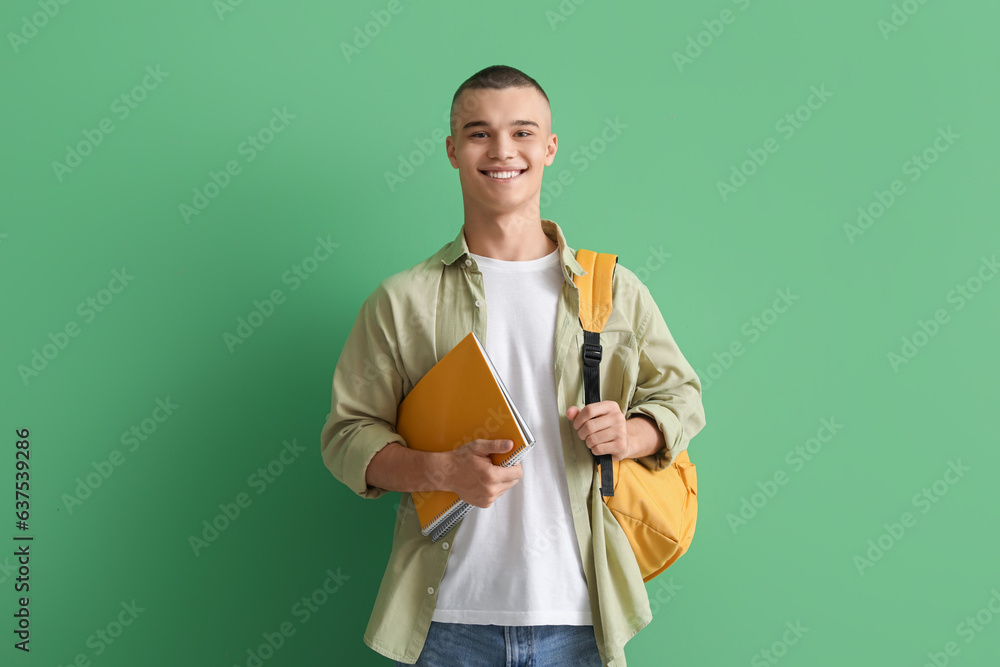 Happy male student with backpack and notebooks on green background