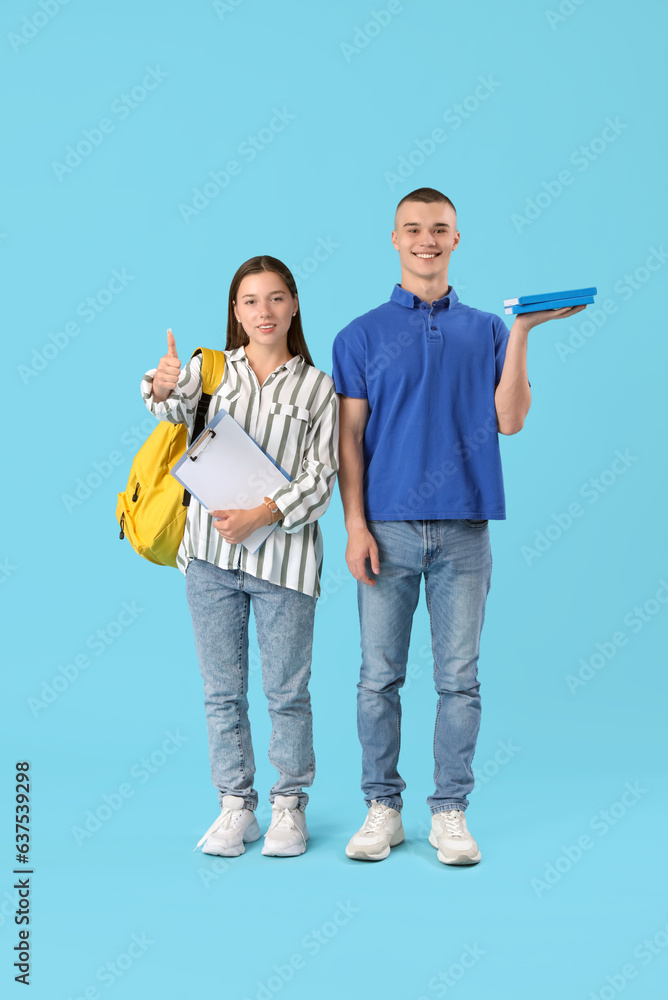 Happy students with clipboard and books showing thumb-up gesture on blue background