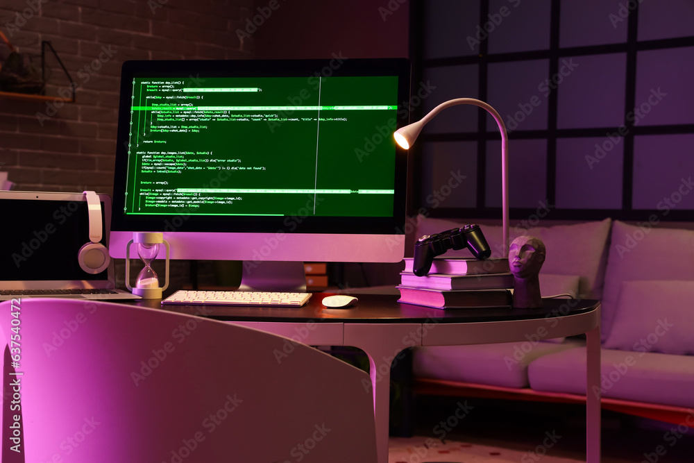 Programmers workplace with computer, laptop and glowing lamp in dark office