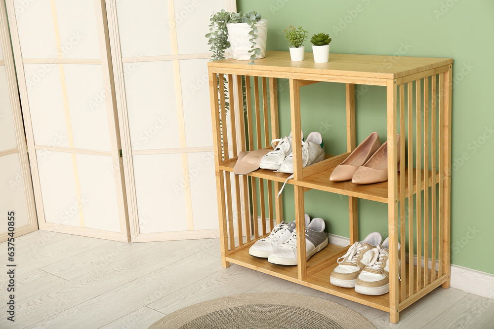 Wooden shoe rack with shoes, orthopedic insoles and houseplants near color wall