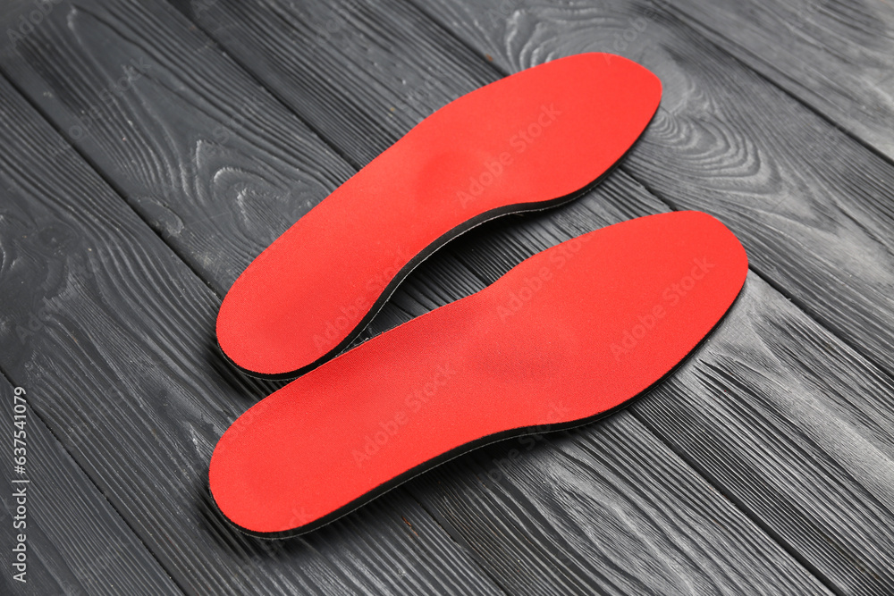 Pair of red orthopedic insoles on dark wooden background