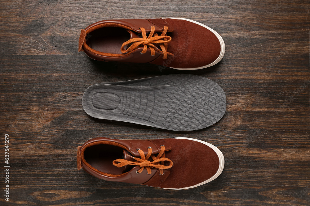 Pair of stylish shoes and orthopedic insoles on dark wooden background