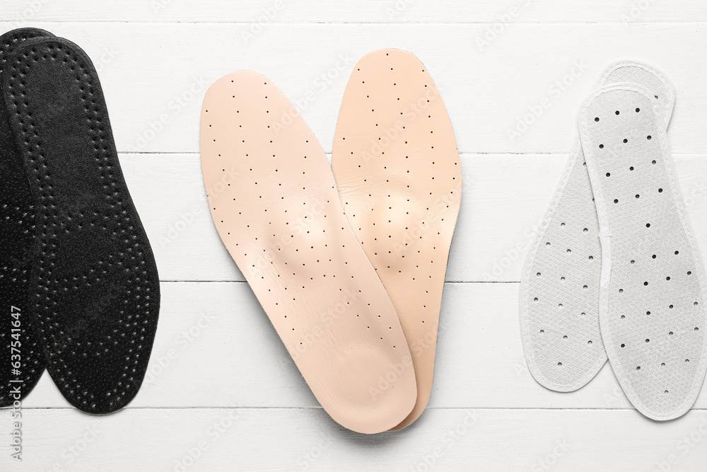 Set of different orthopedic insoles on light wooden background