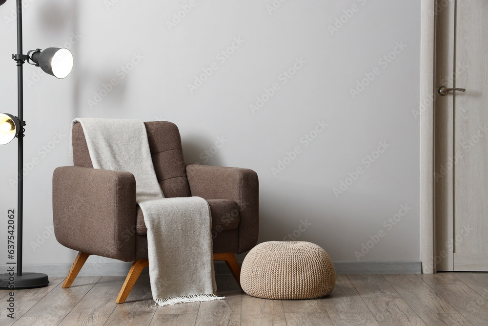 Interior of living room with soft armchair, pouf and glowing lamp