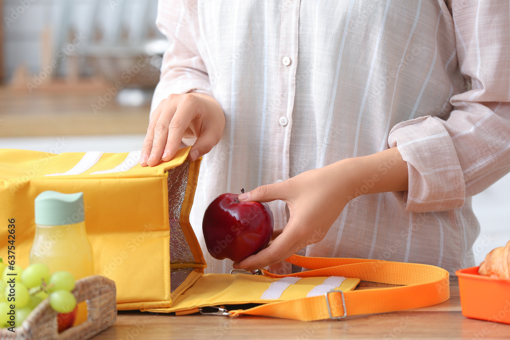 Woman packing fresh meal into lunch box bag in kitchen