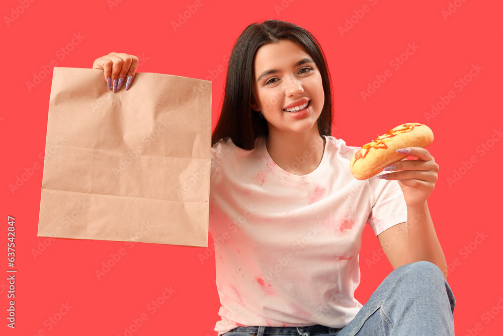 Pretty young woman with tasty hot dog and bag on red background. Food delivery concept