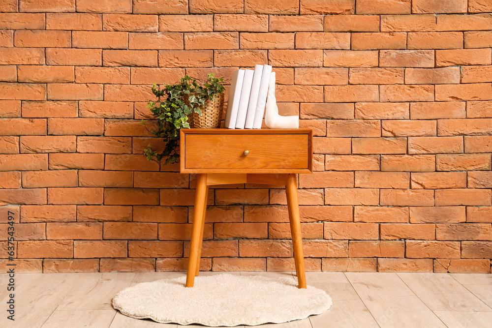 Holder with books and houseplant on table near brick wall in room