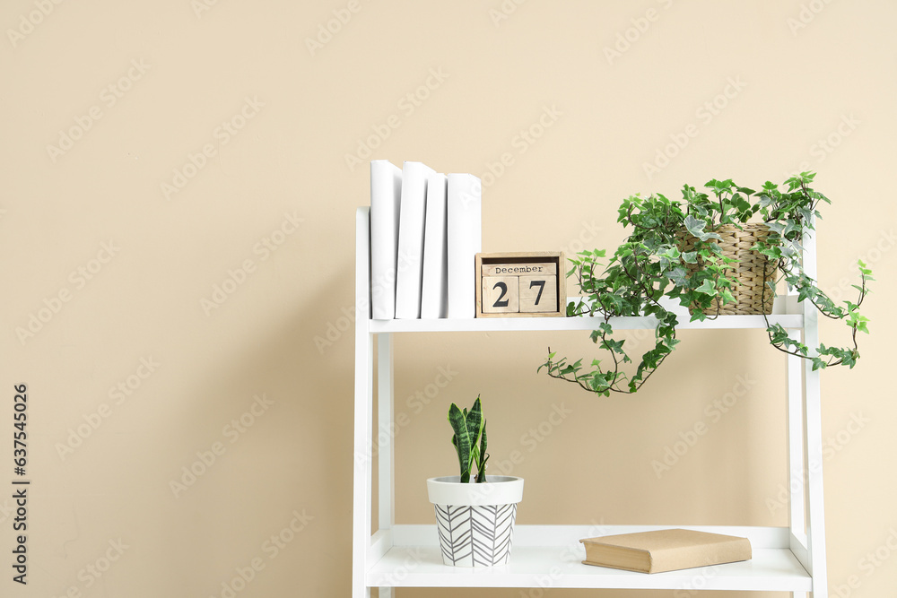 Shelving unit with books and houseplants near beige wall