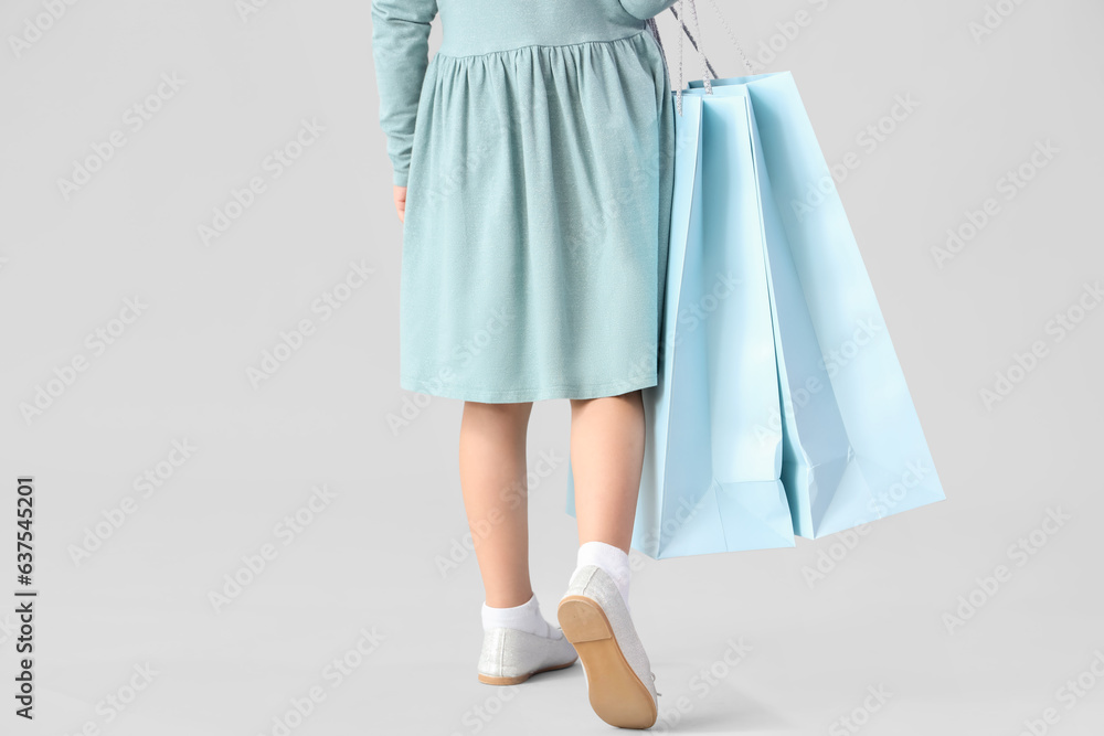 Cute little girl with shopping bags on light background, back view