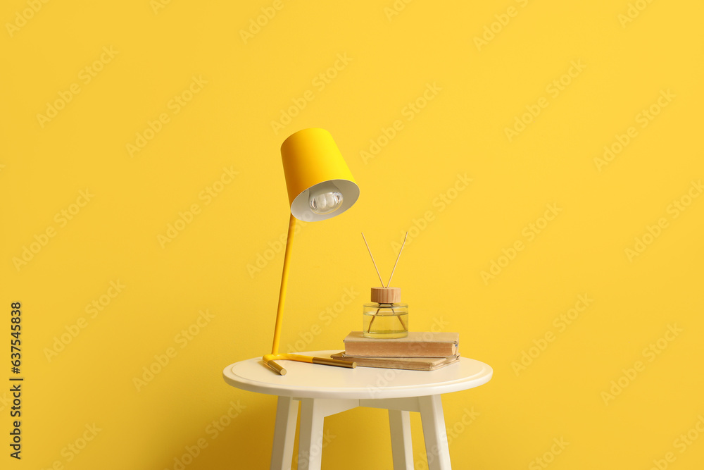 Small table with lamp, books and reed diffuser near yellow wall