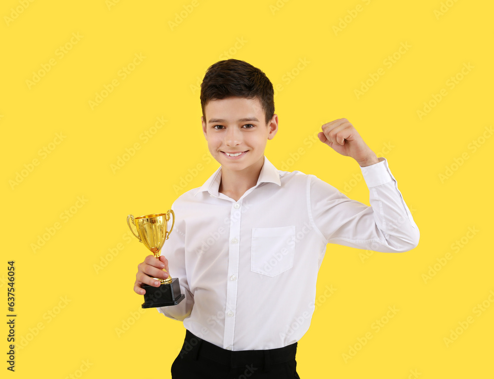 Smart little school boy with prize cup on yellow background