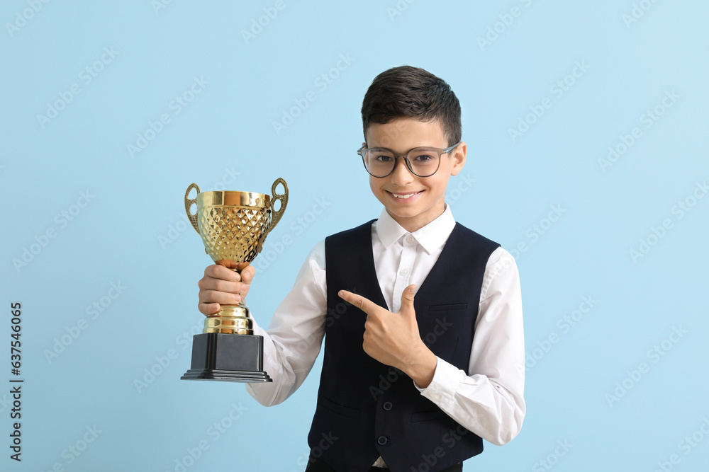 Smart little school boy with prize cup on light blue background